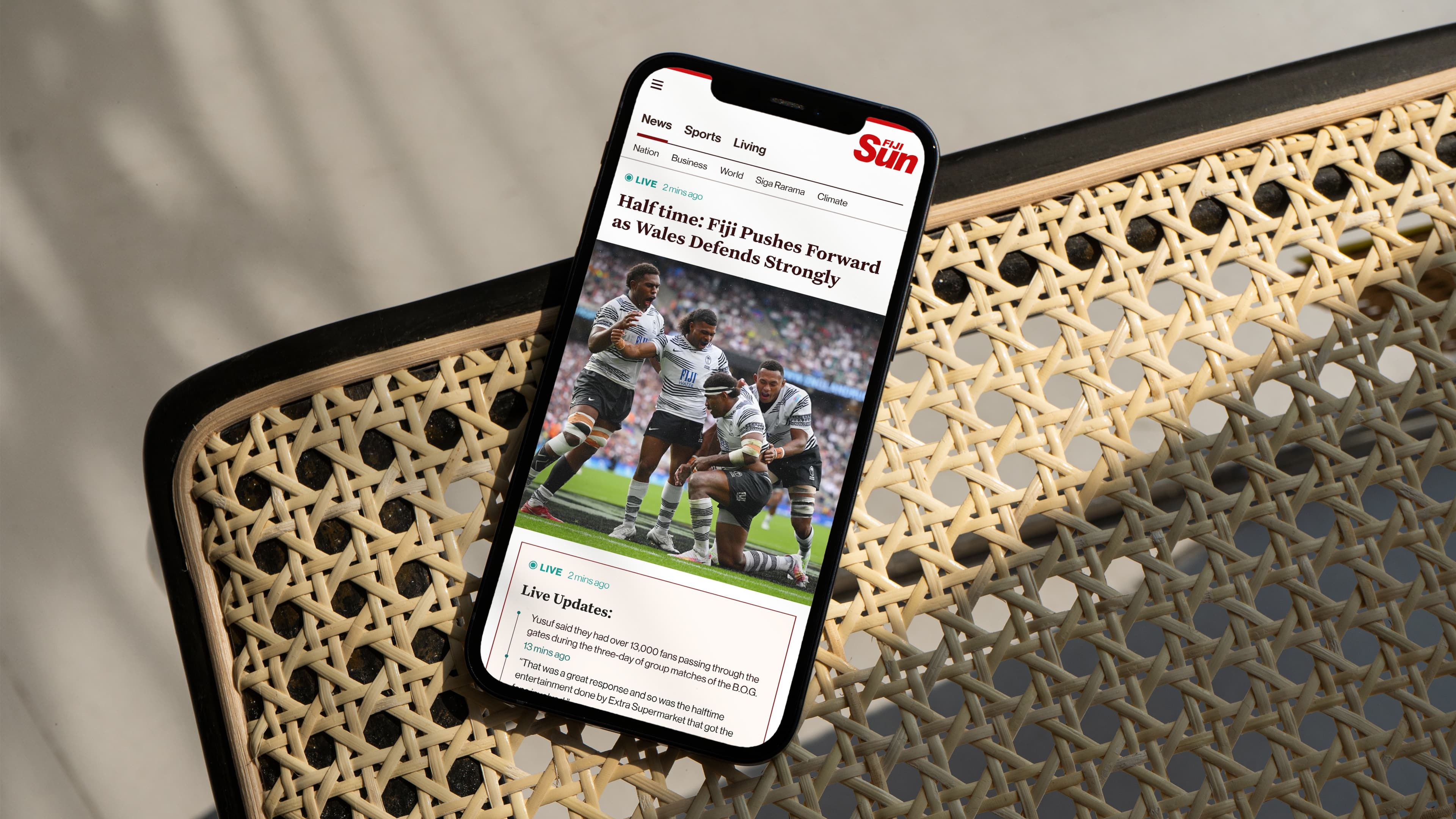 A mobile phone on a rattan chair with The Fiji sun live sports section open on the screen 